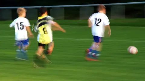 Varios ni&ntilde;os juegan a f&uacute;tbol en un campo de hierba.