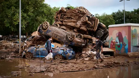 Dos personas caminan delante de varios coches destruidos por la DANA en Alfafar. PABLO LASAOSA