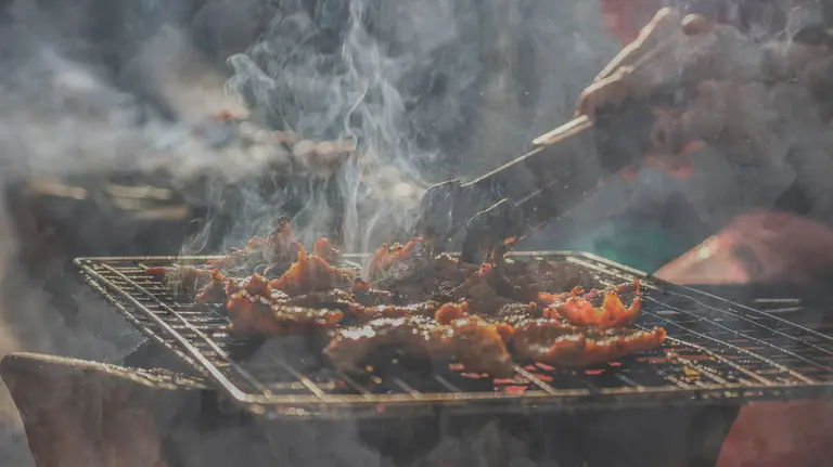 Una persona prepara una barbacoa con mucho humo. ARCHIVO
