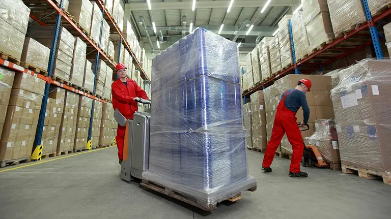 Unos operarios manejan una transpaleta para transportar un paquete de gran tonelaje en un almacén. ARCHIVO