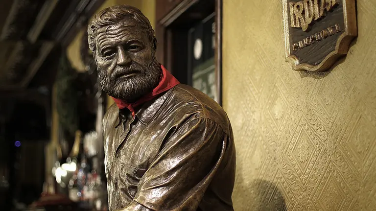 GRAF9791. PAMPLONA 01/12/2018.- La escultura de Ernest Hemingway luce el tradicional "pa&ntilde;uelico" de San Ferm&iacute;n en el popular Caf&eacute; Iru&ntilde;a de la Plaza del Castillo de Pamplona. Esta plaza acoge la exposici&oacute;n "Recuperando a Hemingway" donde se muestran algunas fotograf&iacute;as in&eacute;ditas y se documentan visitas y rodajes, con im&aacute;genes de Henry Fonda, Orson Welles, Ava Gadner, Deborah Kerr, Gary Cooper, Henry Fonda, Lauren Bacall o Sean Connery por las calles de la capital navarra. El escritor estadounidense protagoniza por tercera edici&oacute;n consecutiva un ciclo de actividades tur&iacute;sticas este a&ntilde;o centradas en su relaci&oacute;n con el cine, y que pretende ofrecer la vertiente "m&aacute;s cultural" de la imagen que proyect&oacute; de la ciudad. EFE/Villar L&oacute;pez