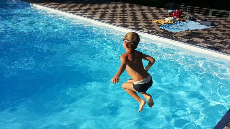Un ni&ntilde;o salta a una piscina desde el bordillo