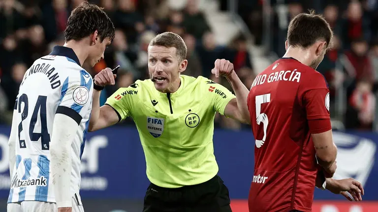 El colegiado Hern&aacute;ndez Hern&aacute;ndez con los jugadores de la Real Sociedad, el franc&eacute;s Robin Le Normand (i) y de Osasuna, David Garc&iacute;a, durante el encuentro correspondiente a los octavos de final de la Copa del Rey que disputan hoy mi&eacute;rcoles Osasuna y Real Sociedad en el estadio El Sadar, en Pamplona. EFE / Jes&uacute;s Diges.