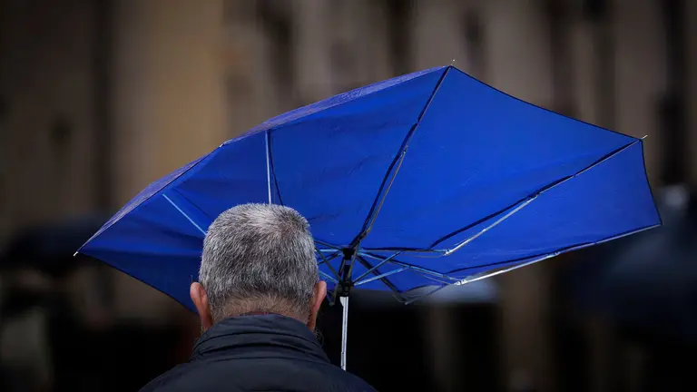 Una persona se protege de una intensa lluvia este viernes en Pamplona en una jornada en la que la vertiente cantábrica de Navarra y el Pirineo se encuentran en aviso amarillo por precipitaciones y acumulación de nieve, una situación que pondría en riesgo la procesión de Viernes Santo de la capital navarra así como otros actos de Semana Santa a lo largo y ancho de la comunidad Foral. EFE/ Villar López