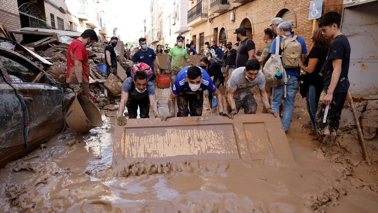 Varias personas retiran el lodo acumulado en una calle de la localidad valenciana de Paiporta, este s&aacute;bado. .EFE/ Biel Alino