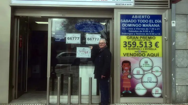 Luis Miguel Arambarri ante la puerta de su punto de venta de loter&iacute;as y con los n&uacute;meros premiados que &eacute;l ha vendido. CEDIDA