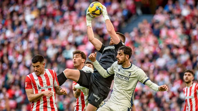 El portero del Athletic Club de Bilbao Unai Simón (c) atrapa el balón ante el defensa del Osasuna Alejandro Catena (d), durante el partido de la jornada 29 de LaLiga que Athletic Club y Atlético Osasuna disputan este domingo en el estadio de San Mamés. EFE/Javier Zorrilla