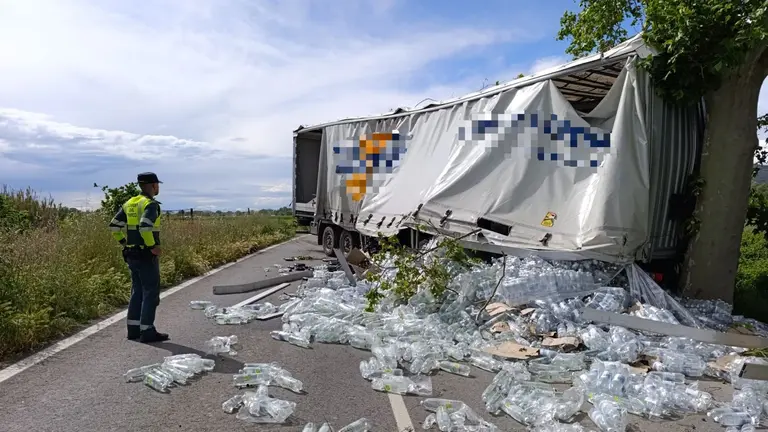 Las botellas eparcidas por la calzada con el cami&oacute;n atravesado aunte un agente de la Guardia Civil. GUARDIA CIVIL