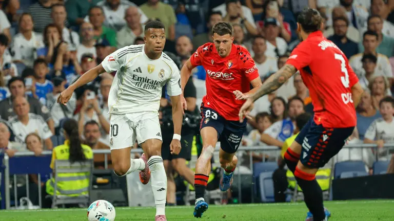 El delantero francés del Real Madrid, Kylian Mbappé (i) controla el balón ante dos rivales de Osasuna en el partido de la primera jornada de LaLiga que Real Madrid y Atlético Osasuna disputan hoy martes en el estadio Santiago Bernabéu. EFE/Mariscal