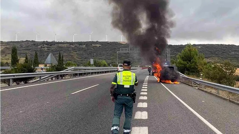 Un agente de la Guardia Civil ante el veh&iacute;culo ardiendo en la subida al Perd&oacute;n por la A-12, en Legarda. GUARDIA CIVIL