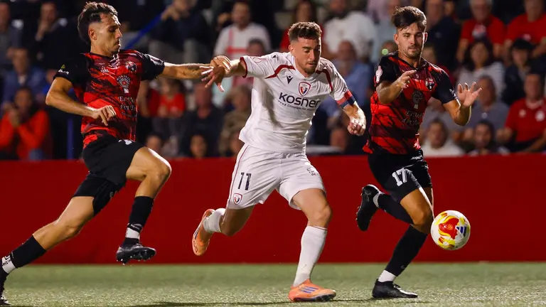 El defensa del Sant Jordi Cameron Ramirez (dcha) pelea un balón con el delantero del Osasuna Kike Barja (c), durante el partido de primera ronda de la Copa del Rey que disputan este miércoles en Palma. EFE/Cati Cladera