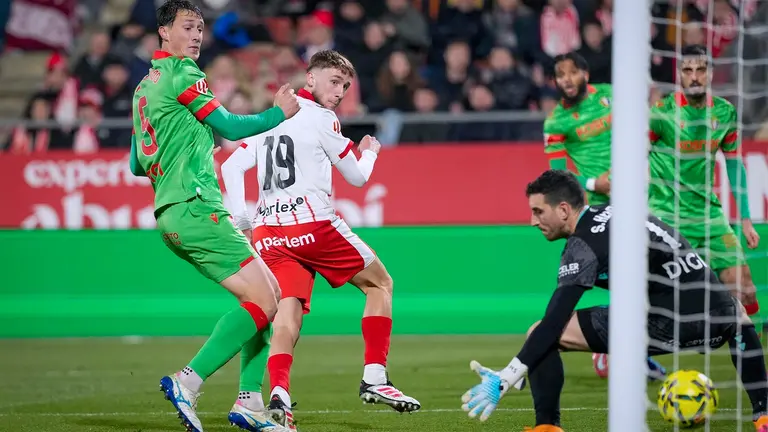 El delantero ucraniano del Girona, Vladyslav Vanat (2i), tras rematar ante el guardameta de Osasuna, Sergio Herrera, para conseguir el primer gol de su equipo durante el encuentro correspondiente a la jornada 19 de Laliga EA Sports que disputan hoy s&aacute;bado Girona y Osasuna en el estadio municipal de Montilivi, en la capital gerundense. EFE/David Borrat.