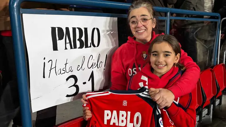 Marta Sola y su hija Sof&iacute;a, con la camiseta de Pablo Inchusta y el cartel que colocaron en la grada de El Sadar para recordarle.
