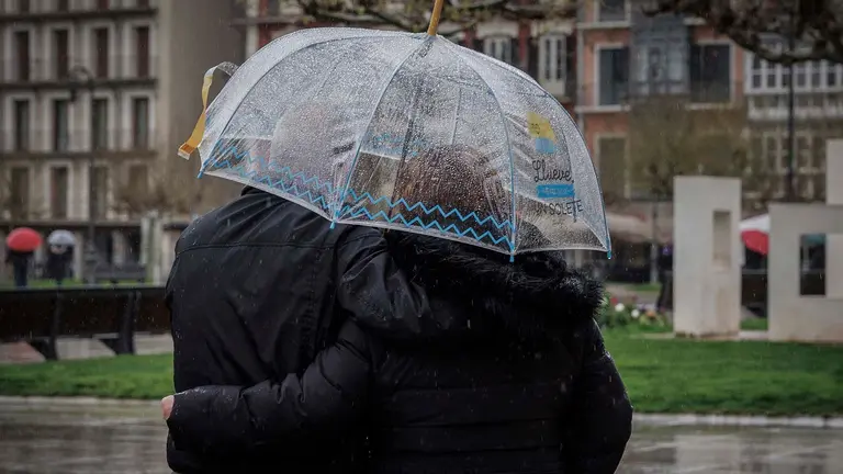 Una pareja se protege de la intensa lluvia que cae este viernes en Pamplona en una jornada en la que la vertiente cantábrica de Navarra y el Pirineo se encuentran en aviso amarillo por precipitaciones y acumulación de nieve, una situación que pondría en riesgo la procesión de Viernes Santo de la capital navarra así como otros actos de Semana Santa a lo largo y ancho de la comunidad Foral. EFE/ Villar López
