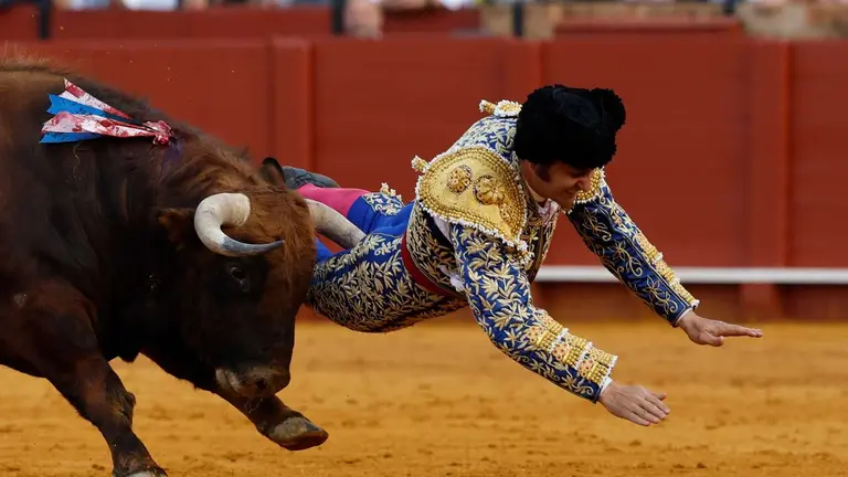 El diestro Morante de la Puebla sufre una cogida durante la novena corrida de la Feria de Abril de Sevilla con reses de la ganader&iacute;a de Hermanos Garc&iacute;a Jim&eacute;nez, este lunes en la plaza de la Maestranza. EFE/ Julio Mu&ntilde;oz