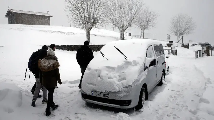 Un grupo de personas pasa ante un vehículo cubierto de nieve aparcado junto al Santuario de San Miguel de Aralar. EFE.