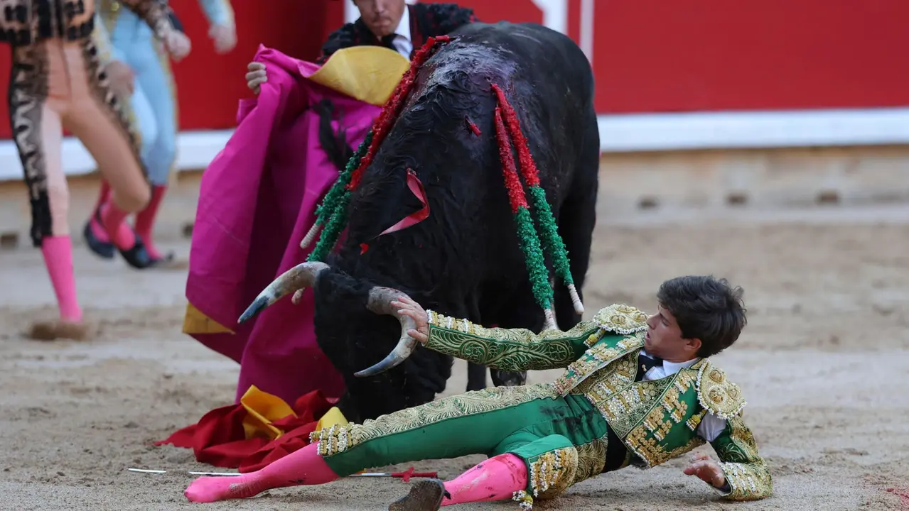 El novillero Aaron Palacio es revolcado por el primero de su lote durante la novillada que con motivo de la Feria del Toro de los Sanfermines 2025 se celebra hoy sábado en la Plaza de Toros de Pamplona, compartiendo cartel con Iker Fernández ´El Mene´ y Bruno Martínez, lidiando reses de la ganadería Pincha, de la localidad navarra de Lodosa. EFE/ J.P Urdiroz