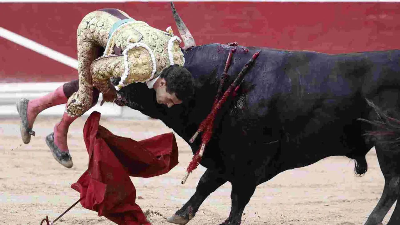 El torero Fernando Adrián sufre un revolcón durante la lidia a su segundo toro de la tarde en la novena de abono de la Feria de Toro de los Sanfermines 2025 con toros de la ganadería gaditana La Palmosilla y en la que comparte cartel con los diestros Jiménez Fortes y Ginés Marín. EFE/Jesús Diges
