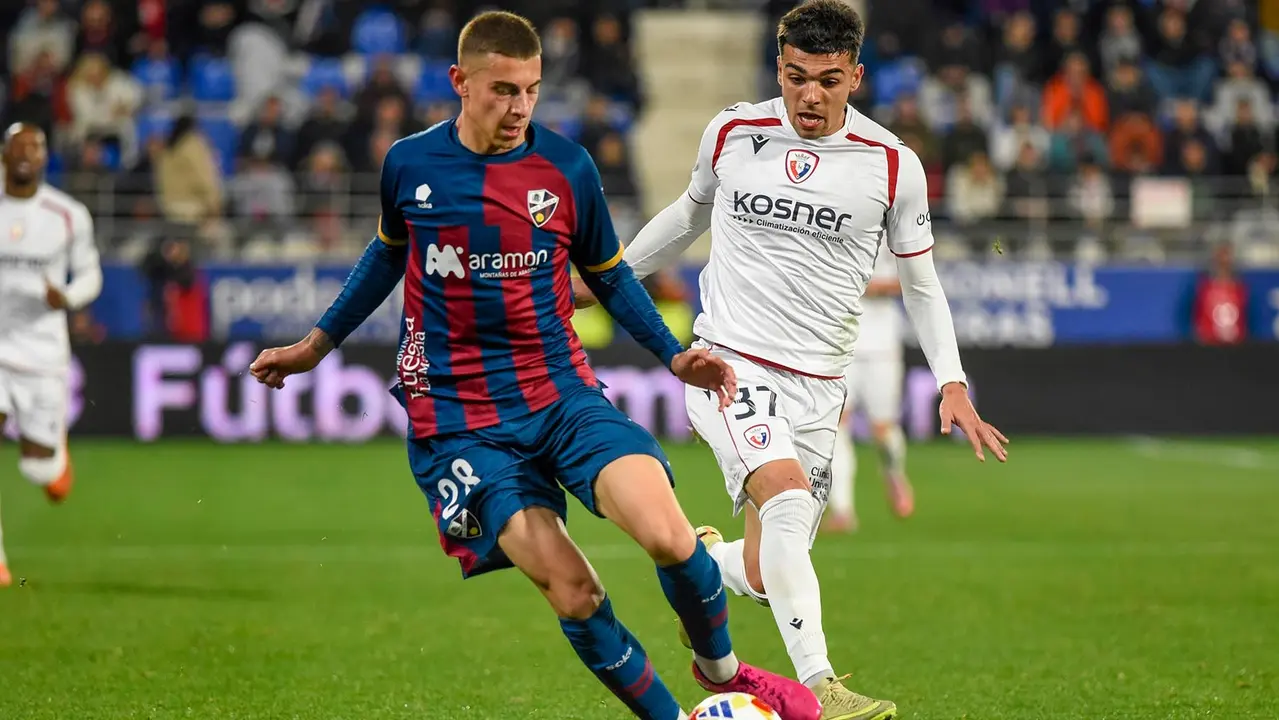 HUESCA , 17/12/2025.- El delantero de Osasuna Robert Arroyo (d) pelea un bal&oacute;n con el defensa del Huesca Sergio Arribas, durante el partido de dieciseisavos de final de la Copa del Rey entre el Huesca y el Osasuna, este mi&eacute;rcoles en el estadio de El Alcoraz, en Huesca. EFE/ Javier Blasco