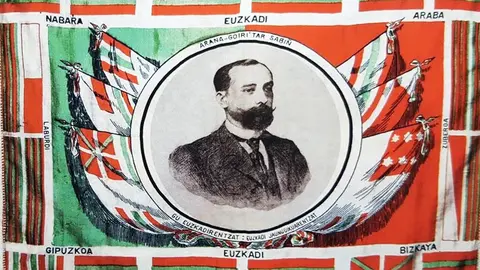 La ikurriña inventada por Sabina Arana Goiri y representada en un pañuelo diseñado por Luis Arana, con la efigie de Sabino Arana_