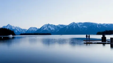 Una pareja contempla un gran lago y montañas nevadas.