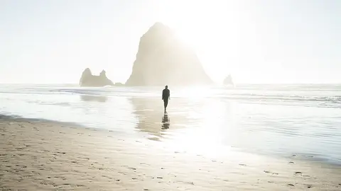 Un hombre pasea por una playa vacía durante un atardecer.
