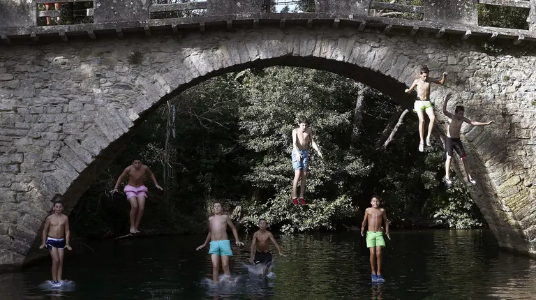 Un grupo de jóvenes saltan desde un puente al agua del río Arga en la localidad de Irotz. EFE/Jesús Diges