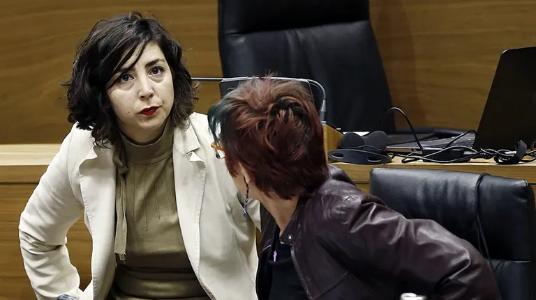 La portavoz del grupo parlamentario de Podemos, Laura Pérez (i), y la parlamentaria de la misma formación Tere Sáez (d), antes de comenzar el pleno de hoy con varias preguntas al Gobierno relacionadas con el departamento de Salud, entre ellas sobre la oferta de empleo público, las jefaturas del Complejo Hospitalario o la reversión de las cocinas. EFE/Jesús Diges