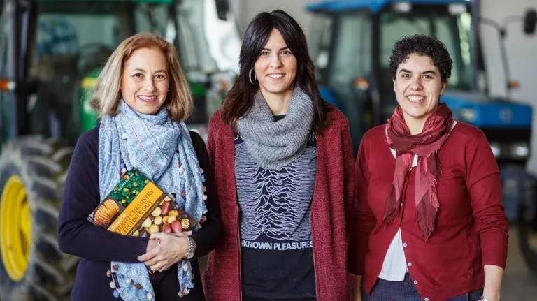 De izq. a dcha. Carmen Jarén, con el libro, Ainara López y Silvia Arazuri, en la Finca de Prácticas e Investigación Agrícola de