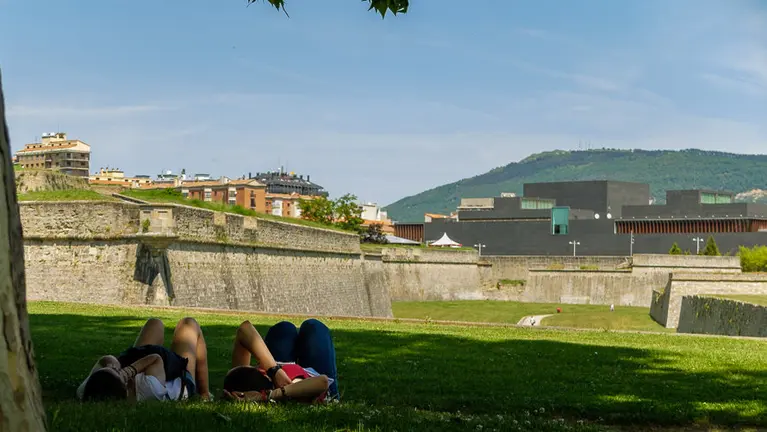 Tiempo. Dos jóvenes tumbadas a la sombra de un árbol en la Vuelta del Castillo de Pamplona.   IÑIGO ALZUGARAY