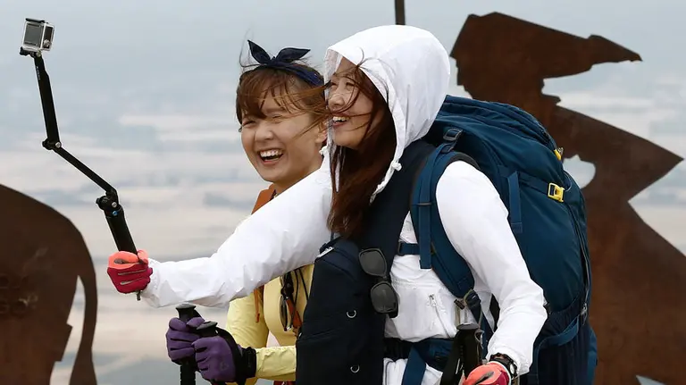 Dos peregrinas se hacen una fotografía en el alto de El Perdón donde sopla un fuerte viento en un día con tiempo fresco y revuelto. EFE/JESÚS DIGES