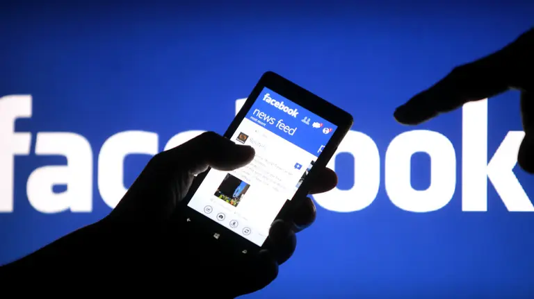 Una persona sujeta un móvil con la aplicación de Facebook abierta.
