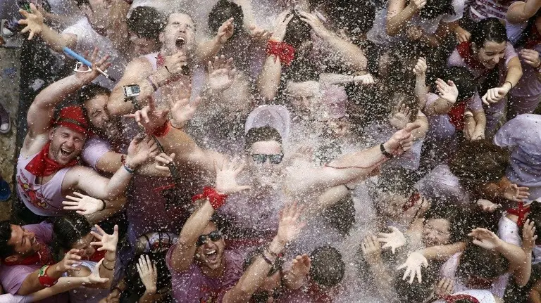 Un grupo de personas abre sus brazos para recibir agua desde un balcón tras el lanzamiento del tradicional Chupinazo desde el balcón del Ayuntamiento de Pamplona. EFE. JESÚS DIGES