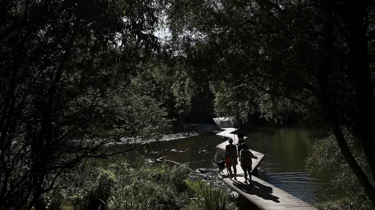 Un grupo de personas atraviesan unas pasarelas sobre el rio Arga bajo un intenso sol. Las imágenes del tiempo marcado por el calor vivido en Pamplona. EFE/Jesús Diges
