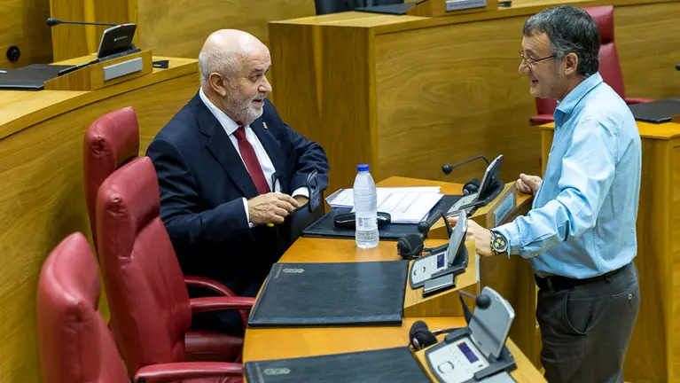 El consejero de Educación, José Luis Mendoza, charla durante el pleno con el parlamentario de Geroa Bai, Patxi Leuza. IÑIGO ALZUGARAY.