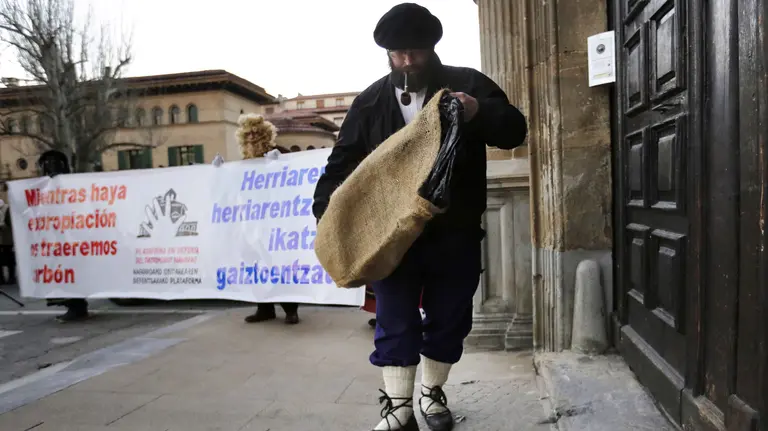 GRA208. PAMPLONA, 30/12/2016.- Una persona que encarna el personaje del Olentzero deposita un saco de carbón frente al palacio episcopal hoy en Pamplona, como un acto en el que la Plataforma de Defensa del Patrimonio navarro ha reivindicado "la devolución" a los pueblos de "todos los bienes inmatriculados por la Iglesia". EFE/Villar López