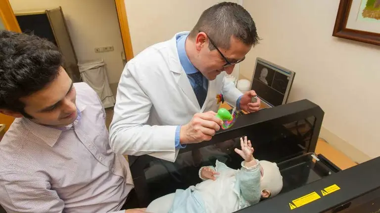 Martín, padre de un niño con plagiocefalia, junto al responsable del Taller Ortopédico de la Clínica, Álvaro de Pablos, durante el escáner para hacer la medición del cráneo del bebé. CUN
