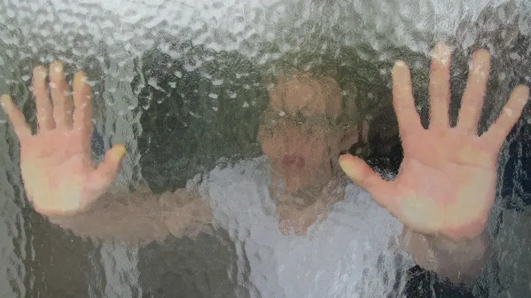 Un hombre contra el cristal de una ventana.