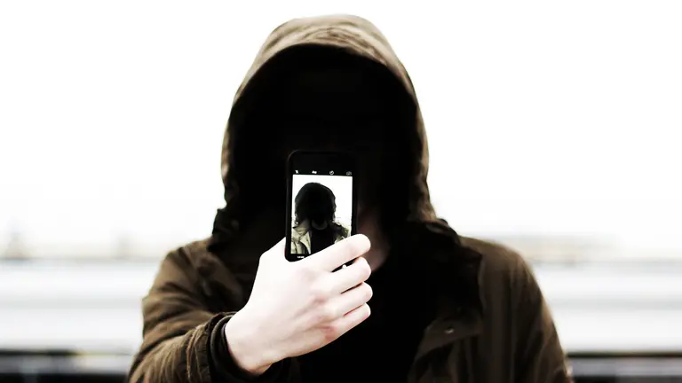 Un joven con una capucha sujeta un móvil