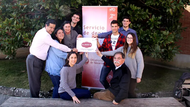 Varios de los organizadores de la Universidad de Navarra posan junto al cartel que demuestra la cantidad reunida tras la celebración de esta carrera.jpg