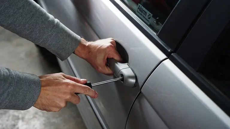 Un hombre forzando la cerradura de un coche para robar.