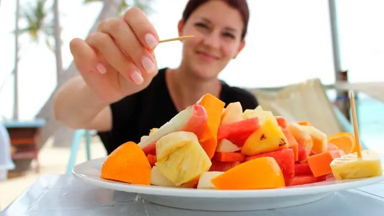 Mujer comiendo un plato de varias piezas de fruta en una terraza. EP