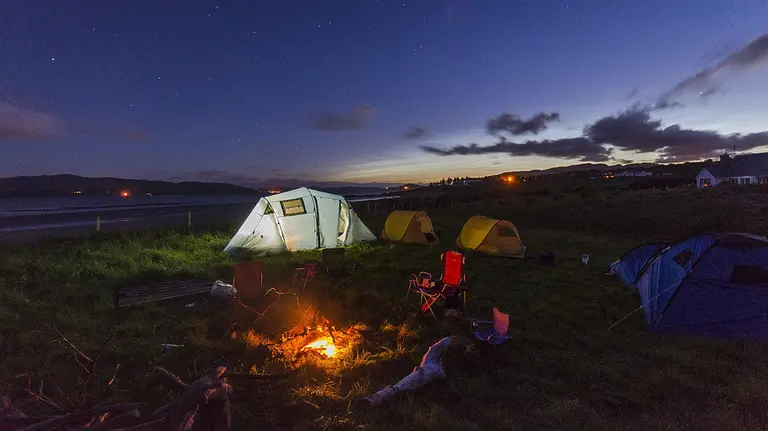 Imagen de un camping y varias tiendas de campaña junto a una hoguera encendida cerca de la playa ARCHIVO