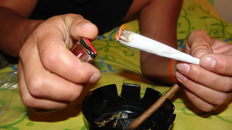 Un hombre encendiéndose un porro de marihuana.