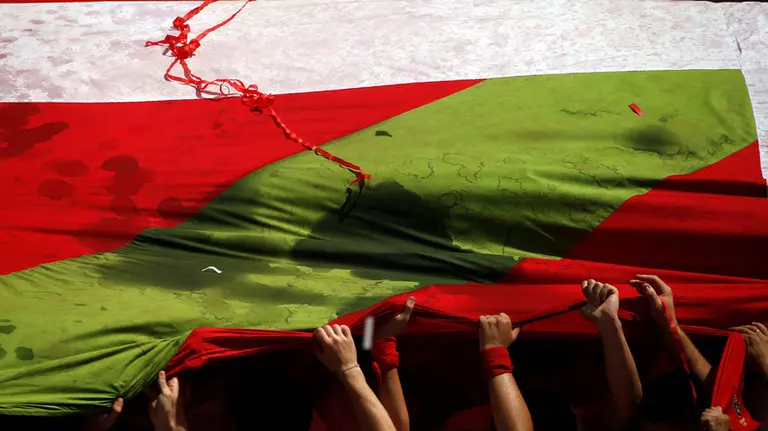 Varias personas despliegan una ikurriña gigante en la plaza del Ayuntamiento instantes previos al Chupinazo de San Fermín. REUTERS