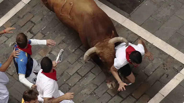 GRA020. PAMPLONA, 13/07/2017.- Un toro de la ganadería gaditada de Núñez del Cuvillo arrolla a un mozo en el tramo inicial de la calle Estafeta, durante el séptimo encierro de los San Fermines 2017, en el que las reses han protagonizado una rápida carrera de dos minutos y diez segundos hasta la arena de la plaza, y en la que, hasta el momento, se han contabilizado dos heridos por asta y un contusionado. EFE/Juan Pedro Urdíroz