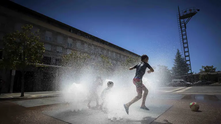 Unos niños se divierten con el agua de una fuente de Pamplona, en una jornada en la que las temperaturas han alcanzado los 33 grados en la capital navarra y el cielo aparece completamente despejado. EFE/Villar López