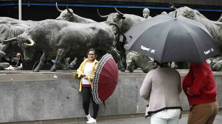 Un grupo de turistas se fotografían junto al Monumento al Encierro en Pamplona en una jornada donde las temperaturas, que no sobrepasan los 15 grados, y la lluvia hacen que el día sea mas típico del otoño que de agosto. EFE/Jesús Diges