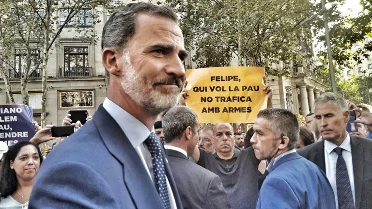 El Rey Felipe VI junto a un manifestante con un cartel en el que vinculaba al jefe de Estado con el tráfico de armas