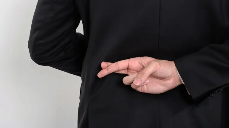 Un hombre cruza sus dedos como signo de falso testimonio en una declaración.